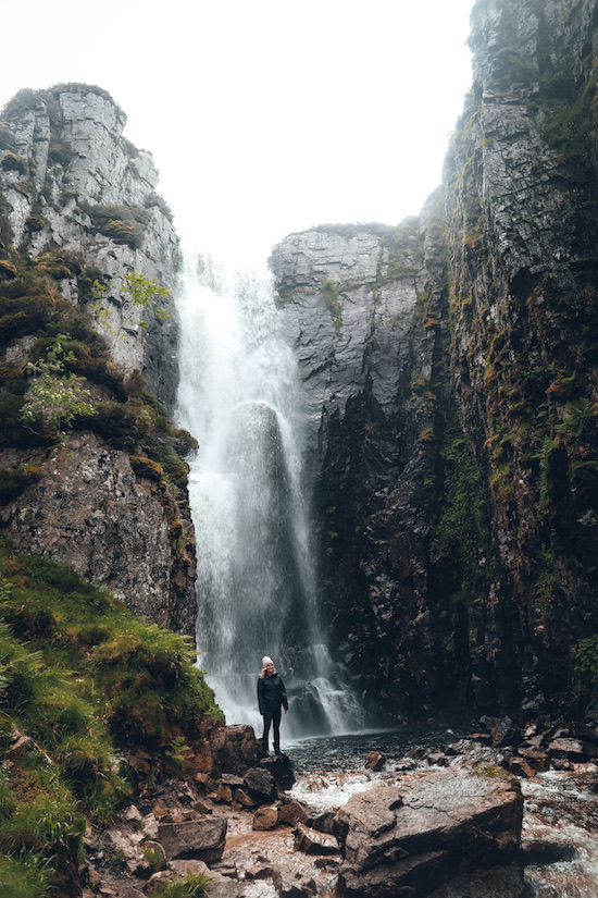 Person steht am Fuße des Clashnessie Waterfalls in Schottland