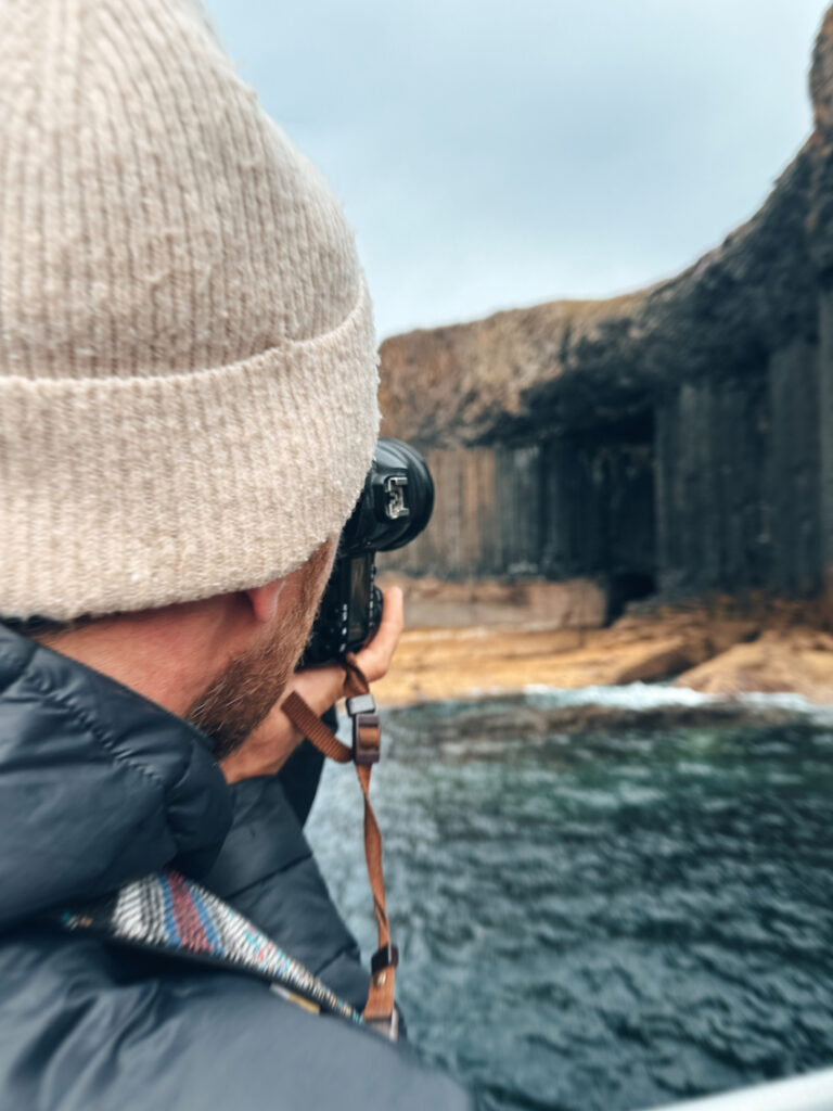 Person mit heller Mütze fotografiert besondere Gesteinsformationen auf der Insel Staffa in Schottland