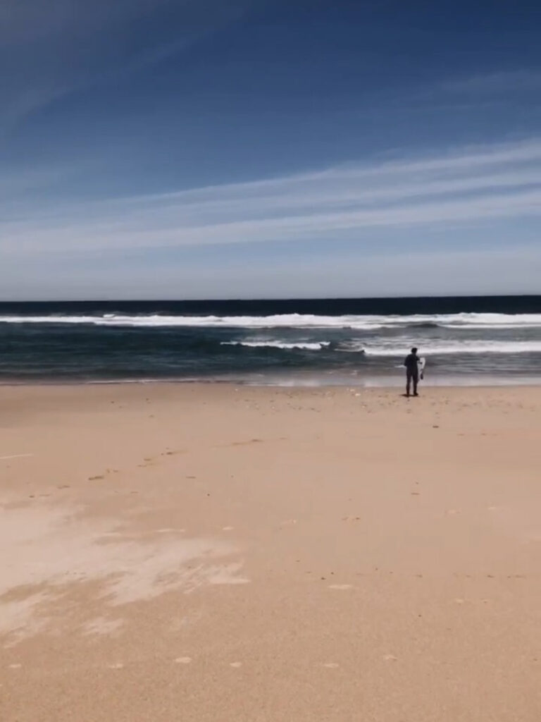Surfer steht am Strand und beobachtet Wellen